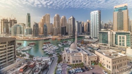 Téléchargez les photos : Yachts à Dubai Marina flanqué de la mosquée Al Rahim et tours résidentielles et gratte-ciel timelapse aérien. Skyline moderne de grande hauteur avec des bateaux et des boutres en bois - en image libre de droit