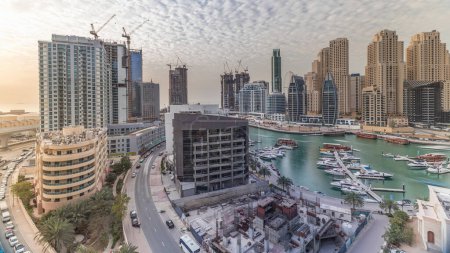 Foto de Yates en Dubai Marina flanqueado por la mezquita Al Rahim y torres residenciales y rascacielos timelapse aéreo. skyline de gran altura moderna con barcos y dhows de madera - Imagen libre de derechos
