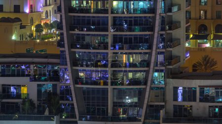 Des rangées de fenêtres lumineuses avec des personnes à l'intérieur de l'immeuble avec balcons la nuit. gratte-ciel moderne avec surface en verre. Concept pour les affaires et la vie moderne. Inclinez-vous
