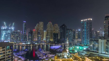 Foto de Yates en Dubai Marina flanqueados por la mezquita Al Rahim y torres residenciales y rascacielos aéreos durante toda la noche con luces apagadas. skyline de gran altura moderna con barcos y dhows de madera - Imagen libre de derechos