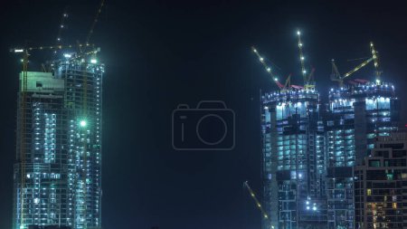 Photo for Aerial view of a skyscraper under construction with huge cranes night timelapse in Dubai marina. Illuminated building. United Arab Emirates - Royalty Free Image