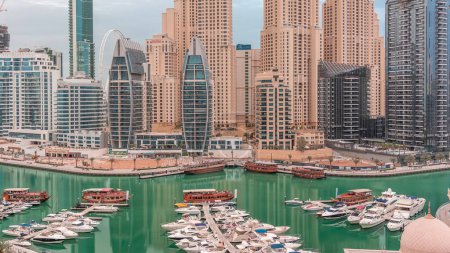 Téléchargez les photos : Yachts de luxe stationnés sur la jetée dans la baie de Dubai Marina avec vue aérienne sur la ville timelapse. Tours et gratte-ciel tôt le matin - en image libre de droit