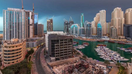 Téléchargez les photos : Tours et gratte-ciel avec des yachts de luxe stationnés sur la jetée dans la baie de Dubai Marina avec vue aérienne sur la ville timelapse. Nuages pluvieux et éclairs. Tôt le matin après le lever du soleil - en image libre de droit