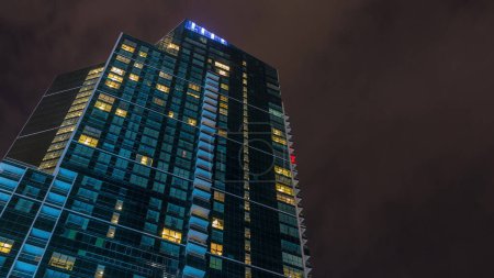 Photo for Night Sky with clouds above modern skyscraper with glowing windows architecture timelapse. Business city center - Royalty Free Image