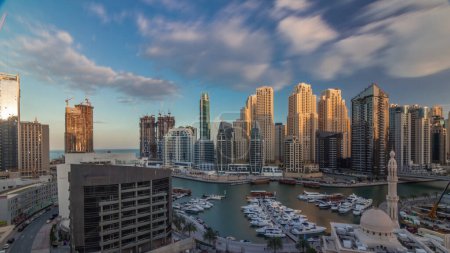 Yachts in Dubai Marina flanked by the Al Rahim Mosque and residential towers and skyscrapers aerial during all day with shadows moving fast. Modern high rise skyline with boats and wooden dhows
