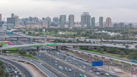 Téléchargez les photos : Terrain de golf de Dubaï avec un paysage urbain des Verts et des districts tecom en arrière-plan transition aérienne du jour à la nuit timelapse. Trafic sur la route Cheikh zayed avec jonction - en image libre de droit