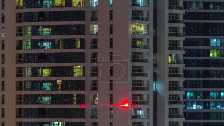 Foto de Filas de ventanas brillantes con personas en el interior del edificio de apartamentos por la noche. Rascacielos moderno de vidrio y hormigón. Concepto de negocio y vida moderna - Imagen libre de derechos