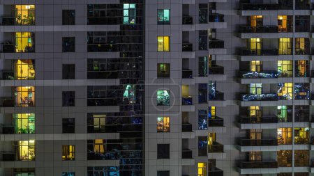 Photo for Rows of glowing windows with people in the interior of apartment building at night. Modern skyscraper from glass and concrete. Concept for business and modern life - Royalty Free Image