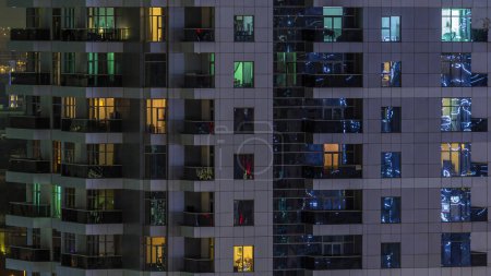 Des rangées de fenêtres rougeoyantes avec des personnes à l'intérieur de l'immeuble la nuit. gratte-ciel moderne en verre et béton. Concept pour les entreprises et la vie moderne

