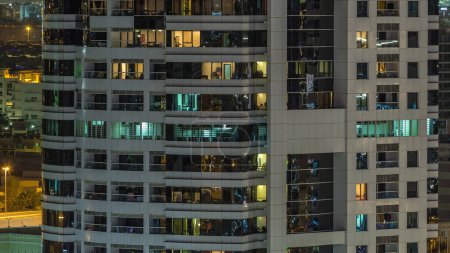 Téléchargez les photos : Des rangées de fenêtres rougeoyantes avec des personnes à l'intérieur de l'immeuble la nuit. gratte-ciel moderne en verre et béton. Concept pour les entreprises et la vie moderne - en image libre de droit