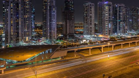 Aerial panoramic view to Sheikh Zayed road from Dubai Marina with JLT illuminated skyscrapers night timelapse, Dubai. Traffic and metro station. United Arab Emirates