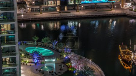 Téléchargez les photos : Promenade au bord de l'eau avec piscine à Dubai Marina timelapse de nuit aérienne. Bateaux et yachts flottant sur le canal. Dubai, Émirats arabes unis - en image libre de droit