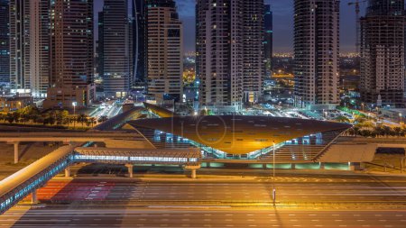 Foto de Vista aérea a Sheikh Zayed carretera desde Dubai Marina con JLT rascacielos iluminados noche a día timelapse transición, Dubai. Tráfico, pasarela y estación de metro. Emiratos Árabes Unidos - Imagen libre de derechos