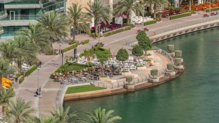 Photo for Waterfront promenade with restaurant in Dubai Marina aerial timelapse. Boats and yachts floating on canal. Dubai, United Arab Emirates - Royalty Free Image