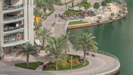 Téléchargez les photos : Promenade au bord de l'eau avec palmiers à Dubai Marina timelapse aérienne. Bateaux et yachts flottant sur le canal. Dubai, Émirats arabes unis - en image libre de droit