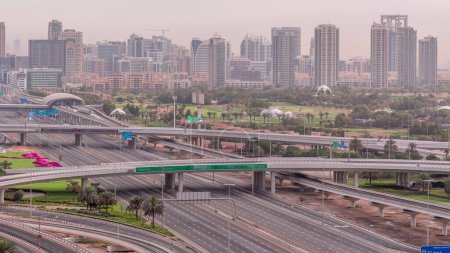 Téléchargez les photos : Terrain de golf de Dubaï avec un paysage urbain des Verts et des districts tecom à l'arrière-plan intemporel aérien. Trafic sur Sheikh zayed route avec jonction et ponts - en image libre de droit