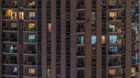 Rows of glowing windows with people in the interior of apartment building at night. Modern skyscraper in the city. Concept for business and modern life