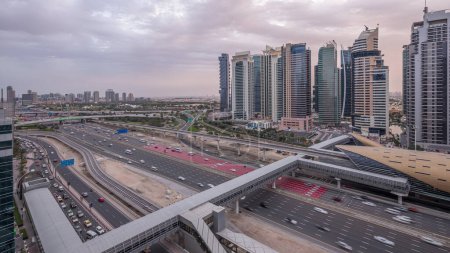 Vista aérea de la parte superior de la carretera Sheikh Zayed rodeado Dubai Marina y JLT rascacielos día a noche timelapse transición, Dubai. Tráfico, puentes y línea de metro. Emiratos Árabes Unidos
