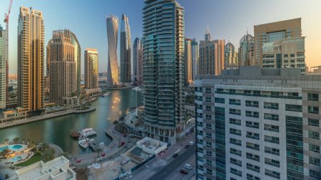 Téléchargez les photos : Vue aérienne des gratte-ciel résidentiels et de bureau de Dubai Marina avec timelapse en bord de mer. Matin après le lever du soleil avec des ombres se déplaçant rapidement. Soleil réfléchi par le verre. Bateaux et yachts flottants - en image libre de droit