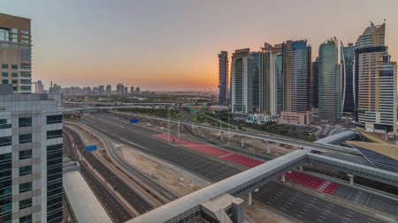 Foto de Vista aérea del amanecer a la carretera Sheikh Zayed desde Dubai Marina con rascacielos JLT timelapse, Dubai. Tráfico y estación de metro. Cielo naranja con sol detrás de torres. Emiratos Árabes Unidos - Imagen libre de derechos