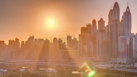 Dubai Marina skyscrapers and golf course sunset timelapse, Dubai, United Arab Emirates. Aerial view from Greens district. Rays of light and orange sky
