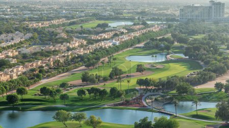 Téléchargez les photos : Vue aérienne sur les villas et les maisons avec terrain de golf avec pelouse verte et les lacs timelapse. Trafic dans les rues. Lumière chaude du soir - en image libre de droit