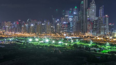 Photo for Dubai Marina illuminated skyscrapers and golf course night timelapse, Dubai, United Arab Emirates. Aerial view from Greens district - Royalty Free Image
