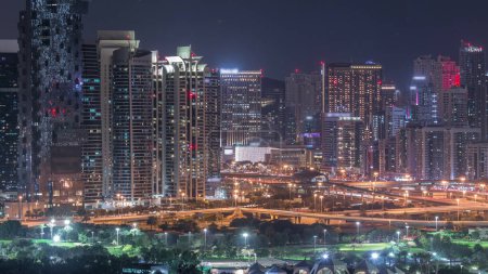 Jumeirah lake towers illuminated skyscrapers and golf course night timelapse, Dubai, United Arab Emirates. Aerial view from Greens district