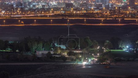 Téléchargez les photos : Vue aérienne sur les villas et les maisons près du golf nuit timelapse. Désert et chantier de construction dans le quartier du cercle du village de Jumeirah sur fond. Trafic sur la route - en image libre de droit