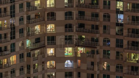 Foto de Ventanas brillantes del edificio de varios pisos con iluminación en el interior y personas en movimiento en apartamentos timelapse. Vista aérea de los modernos rascacielos residenciales en el distrito de Dubai greens - Imagen libre de derechos