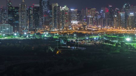Jumeirah lake towers and Dubai marina illuminated skyscrapers and golf course night timelapse, Dubai, United Arab Emirates. Aerial view from Greens district