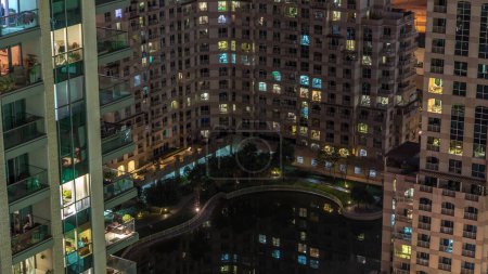 Manmade lake and residential buildings in Greens neighborhood night timelapse in Dubai, UAE. Aerial view from above
