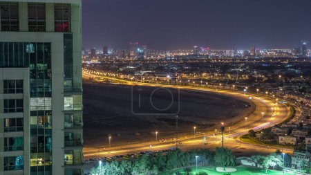 Aerial view to Greens district, villas and houses with Golf course night timelapse. Traffic on intersection. Residential buildings with glowing windows
