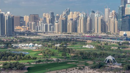 Dubai Marina skyscrapers and golf course morning timelapse, Dubai, United Arab Emirates. Aerial view from Greens district. Green lawn and cloudy sky. Traffic on a highway