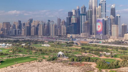 Dubai Marina rascacielos y campo de golf timelapse mañana, Dubai, Emiratos Árabes Unidos. Vista aérea desde el distrito de Greens. Césped verde y cielo nublado
