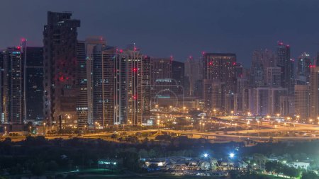 Jumeirah lake towers and Dubai marina skyscrapers and golf course night to day transition timelapse, Dubai, United Arab Emirates. Aerial view from Greens district before sunrise