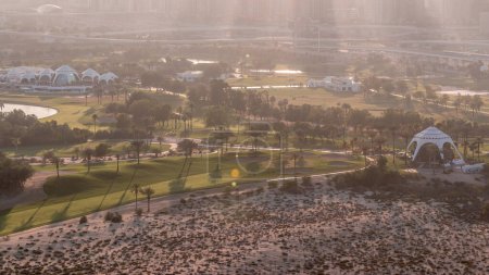 Rays of light on Golf course and Dubai Marina skyscrapers during sunset timelapse, Dubai, United Arab Emirates. Aerial view from Greens district