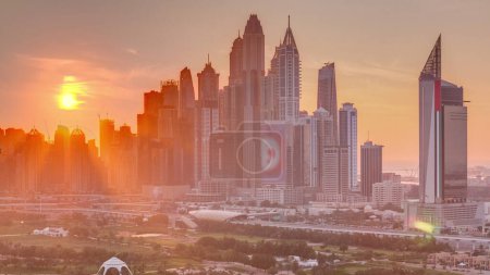 Foto de Dubai Marina rascacielos y campo de golf sunset timelapse, Dubai, Emiratos Árabes Unidos. Vista aérea desde el distrito de Greens. Rayos de luz y cielo naranja - Imagen libre de derechos