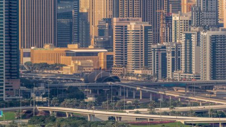 Crossroad and metro station near Dubai Marina and golf course morning timelapse, Dubai, United Arab Emirates. Aerial view from Greens district. Green lawn and traffic on a highway