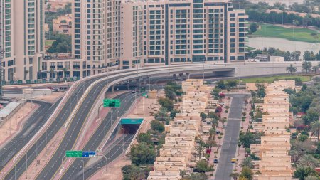 Aerial view of apartment houses and villas in Dubai city timelapse near jumeirah lake towers district, United Arab Emirates. Traffic on the road and overpass. Top view from skyscraper