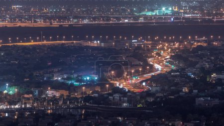 Téléchargez les photos : Vue aérienne des maisons d'appartements et des villas à Dubaï City Night Timelapse près du quartier Jumeirah Lake Towers, Émirats arabes unis. Vue de dessus du gratte-ciel avec la circulation sur la route courbe - en image libre de droit