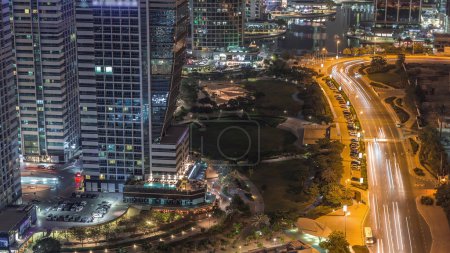 Téléchargez les photos : Jumeirah Lake Towers quartier résidentiel nuit aérienne timelapse près de Dubai Marina. Des gratte-ciel modernes éclairés avec parc et trafic d'en haut - en image libre de droit