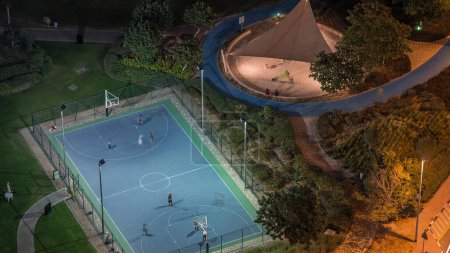 Téléchargez les photos : Terrain de basket-ball au parc dans Jumeirah Lakes Towers timelapse de nuit aérienne, un quartier résidentiel populaire vers l'extrémité sud de Dubaï. Pelouse verte et paumes d'en haut
. - en image libre de droit