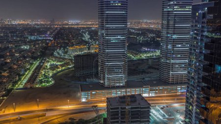 Téléchargez les photos : Jumeirah Lake Towers quartier résidentiel nuit aérienne timelapse près de Dubai Marina. Éclairage des gratte-ciel modernes et de la circulation d'en haut. Villas et maisons sur un fond - en image libre de droit