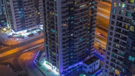 Téléchargez les photos : Vue des tours avec piscine et de la circulation à l'intersection dans la marina de Dubaï depuis le ciel de la nuit. Bâtiments modernes éclairés dans les toits urbains - en image libre de droit
