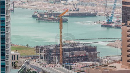 Téléchargez les photos : Vue aérienne d'un gratte-ciel en construction avec d'énormes grues timelapse dans la marina de Dubaï. Navire sur fond. Émirats arabes unis - en image libre de droit