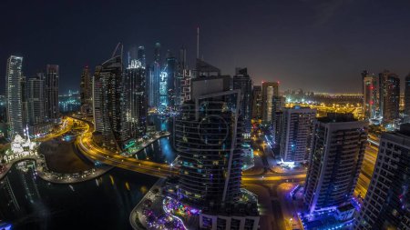 Téléchargez les photos : Vue aérienne panoramique des gratte-ciels résidentiels et de bureau de Dubai Marina avec passage du front de mer de nuit au jour avant le lever du soleil. Bateaux flottants et yachts. Trafic sur une route - en image libre de droit