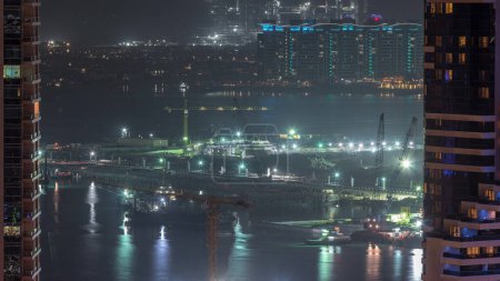 Foto de Vista aérea de los rascacielos del puerto deportivo de Dubái con obras de construcción y la isla Palm Jumeirah en la noche de fondo timelapse. Construcción de una nueva terminal naval - Imagen libre de derechos