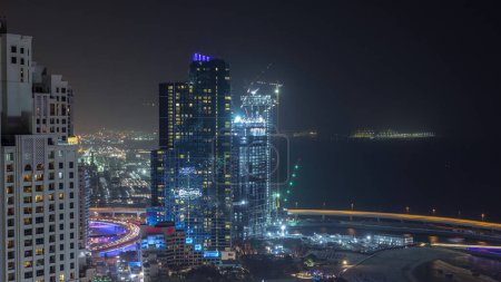 Vista general del paseo marítimo Jumeirah Beach Residence JBR skyline aerial night timelapse with illuminated rascacielos. Tiendas, restaurantes y otros entretenimientos desde arriba con tráfico
