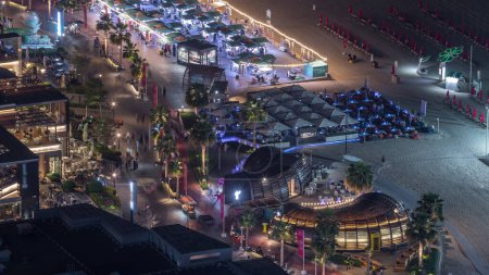 Vista general del paseo marítimo Jumeirah Beach Residence JBR skyline aerial night timelapse with illuminated building. Tiendas, restaurantes y otros entretenimientos desde arriba con tráfico
